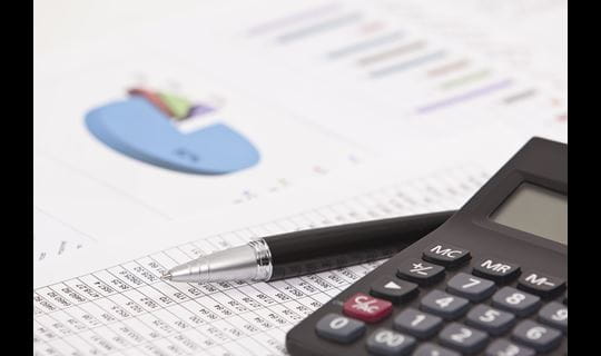 Calculator beside a pen and financial analysis paper